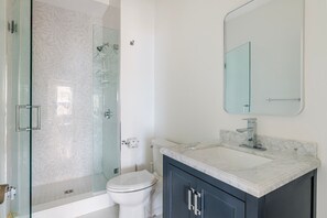 A modern bathroom with a glass-enclosed shower, a white toilet, a marble sink, and dark cabinets. - Blueground | Riverside, washer, nr Charles River (Cambridge)