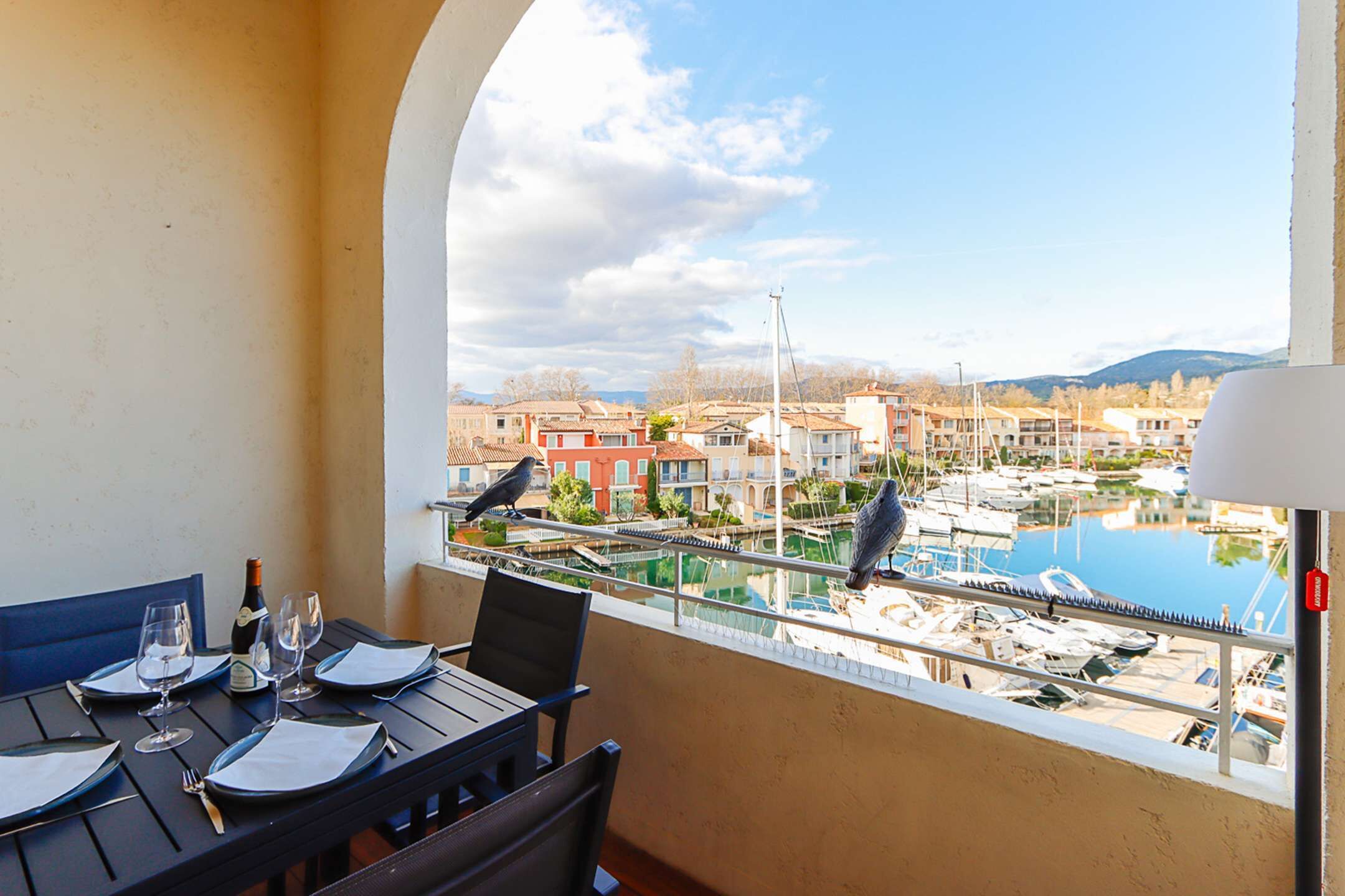 Ein Balkon mit Esstisch, der auf einen Yachthafen mit Booten und Gebäuden im Hintergrund blickt.