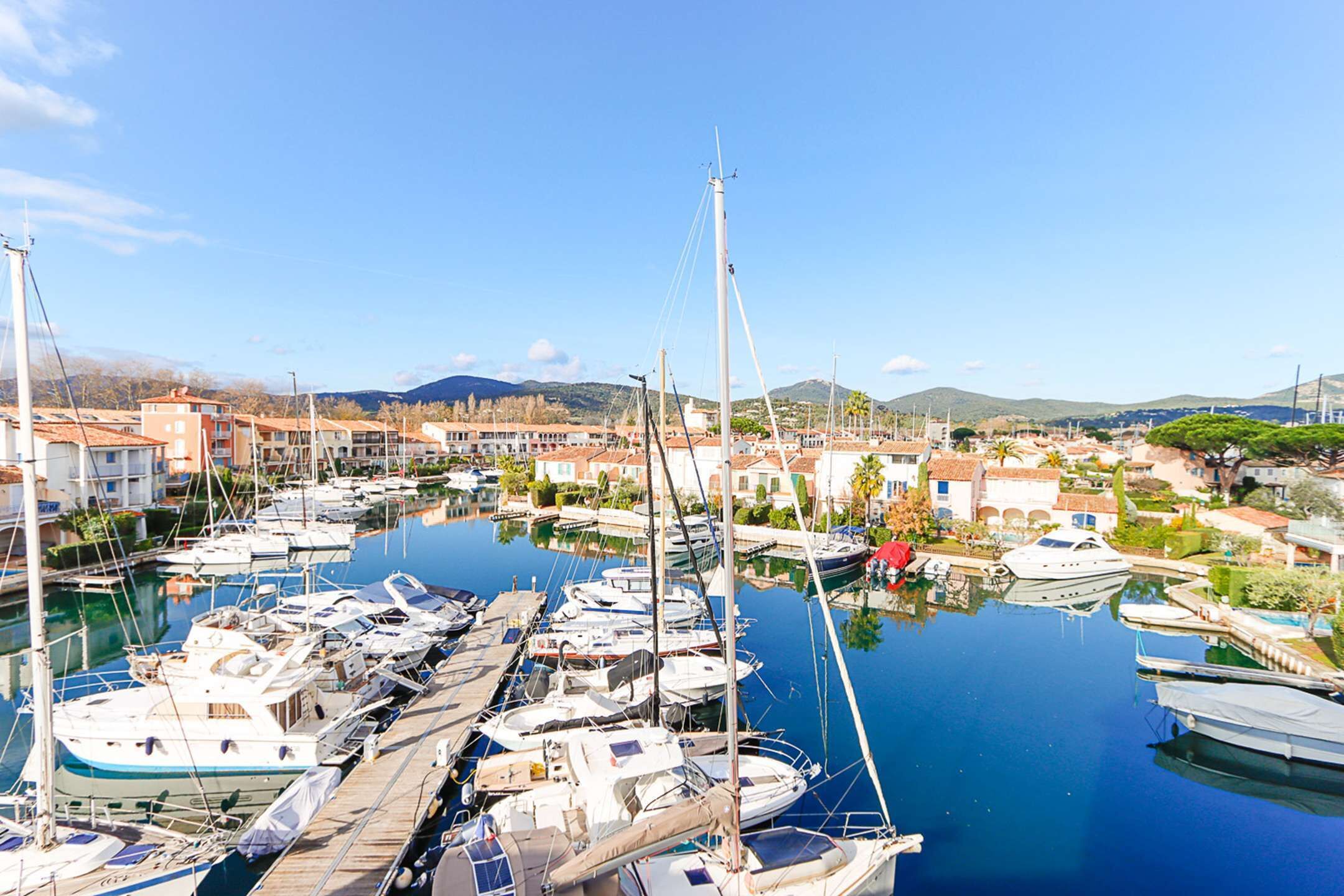 A marina with various boats docked, surrounded by buildings and a clear sky.
