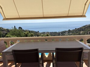 A table with two chairs, a beige canopy, and a view of the sea. - Villa 6 + 2 with pool and air conditioning (LES ISSAMBRES)