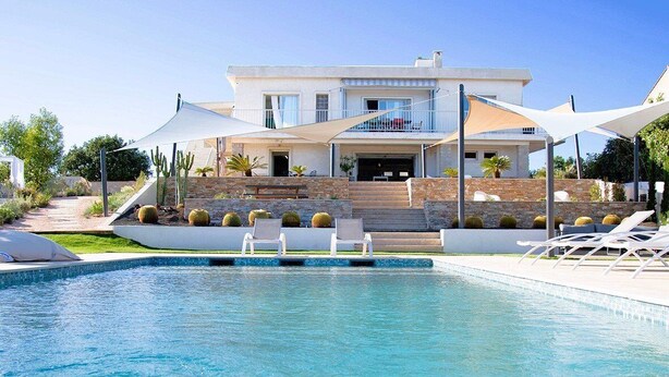 Ett modernt hus med en swimmingpool, utomhusmöbler och kaktusar.