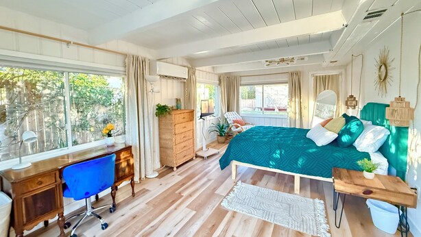 A spacious bedroom with a large bed, a desk, and a chair, featuring wooden flooring and a view of the outdoors. - Quiet , 5 minutes to Tri-City Hospital,fast WiFi, blackout curtains, fenced yard (Vista)