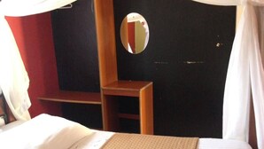 A bedroom with a bed, a nightstand, a mirror, and a window with curtains. - Maya's Guest House (Nyeri)
