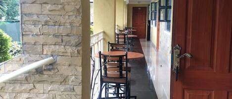A corridor with a stone wall, a wooden door, and a row of tables and chairs.