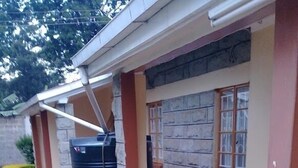 A building with a tiled floor, a stone wall, and a window with a curtain. - Maya's Guest House (Nyeri)