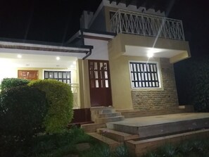 A two-story house with a balcony, a wooden door, and a window with bars. - Maya's Guest House (Nyeri)
