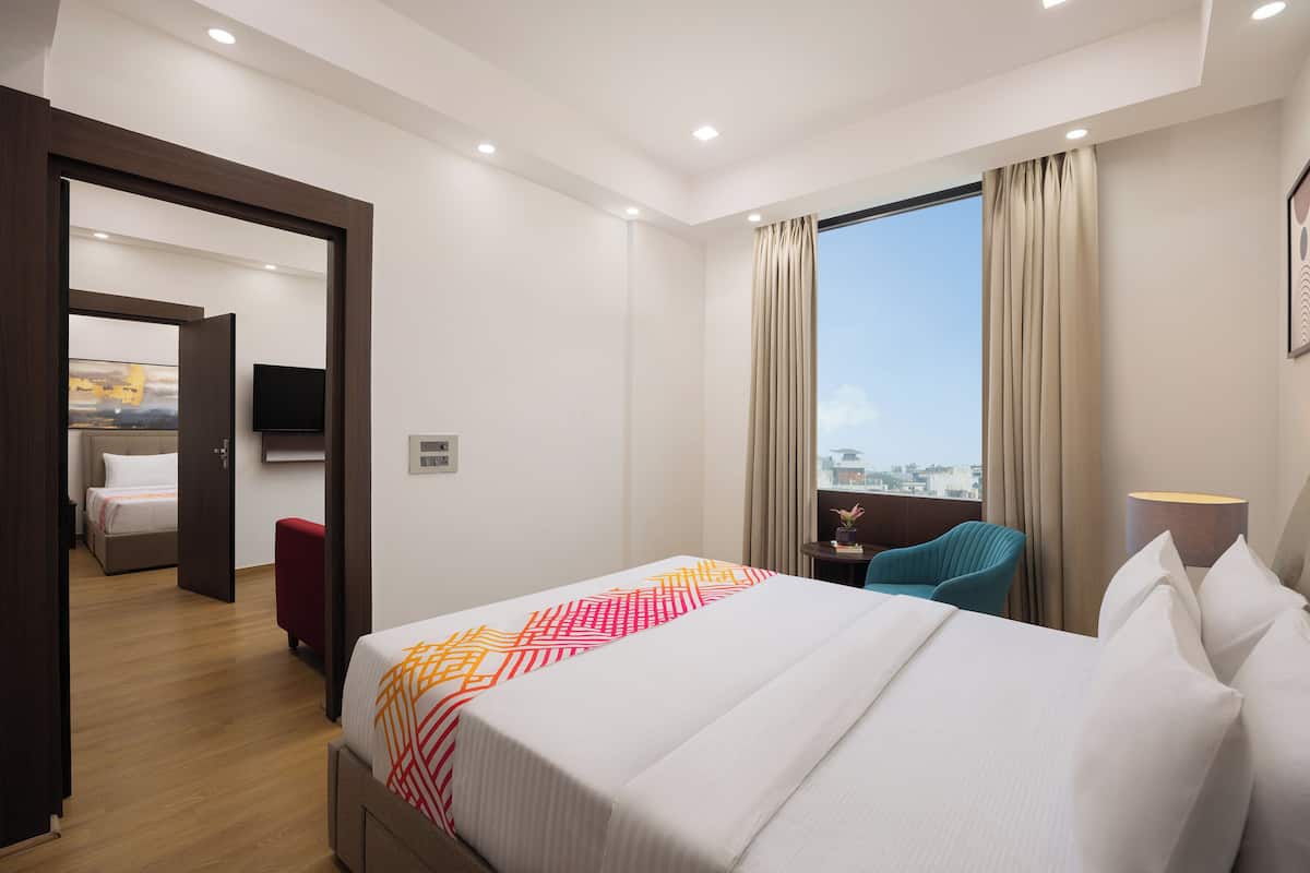 Une chambre d’hôtel avec un grand lit, un bureau avec une chaise, une télévision et une vue sur la ville grâce à une grande fenêtre.