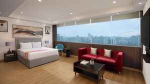 Una habitación de hotel moderna con una cama grande, un sofá rojo, una mesita de centro y vistas a la ciudad a través de amplios ventanales.