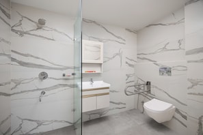 A modern bathroom with marble walls, a glass shower enclosure, a white sink, and a toilet. - Ginger Gurugram Sector 1 (Gurugram)