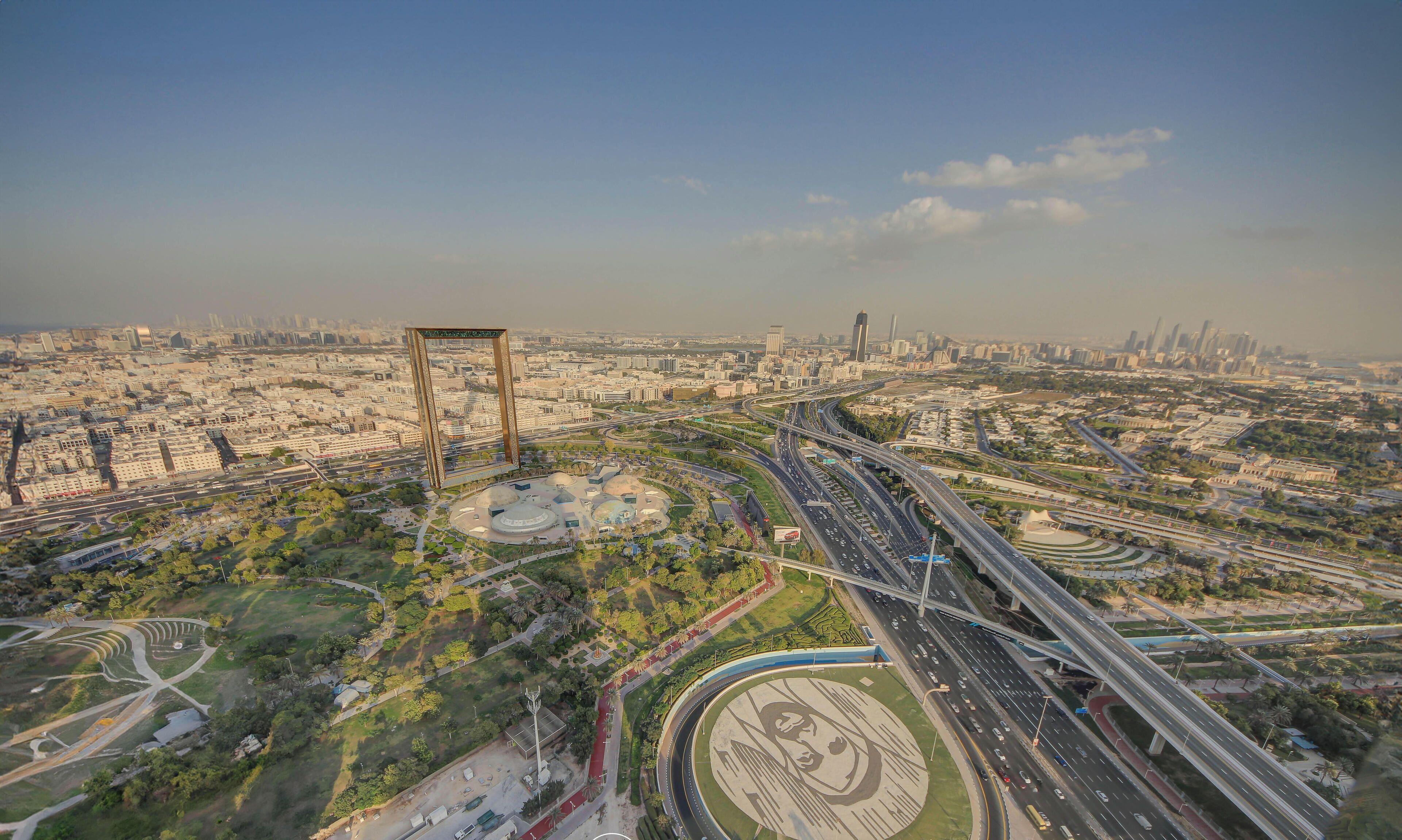 An aerial view of a cityscape with a large, open park area, multiple highways, and a prominent tower structure.