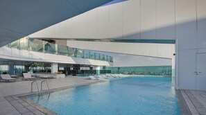Et moderne poolområde indendørs med en pool i glas, liggestole og udsigt over byen.