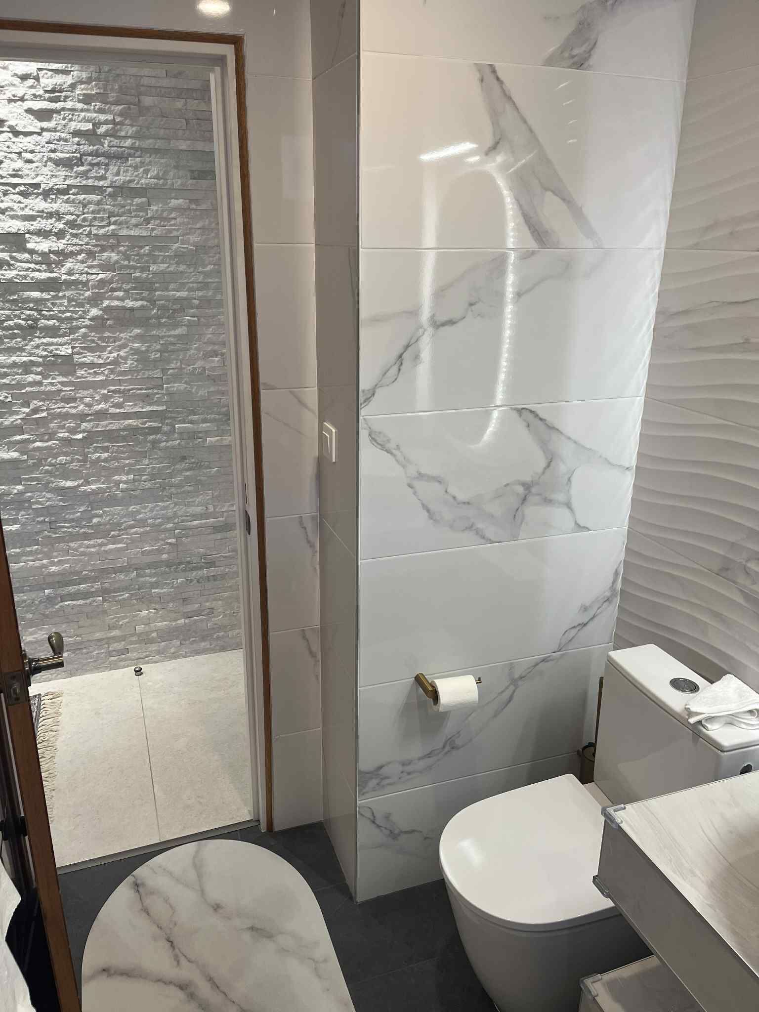 A modern bathroom with a marble wall, a toilet, and a shower area.
