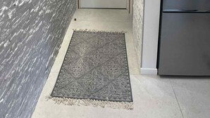 Un pasillo estrecho con pared texturizada, una puerta cerrada, un tapete estampado y un refrigerador de acero inoxidable.