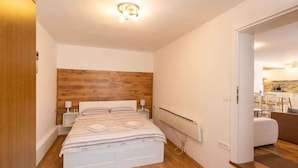 A modern bedroom with a wooden headboard, a white bed, bedside lamps, and a visible radiator. - Holiday flat with terrace (Malinska)