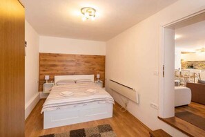 Ein modernes Schlafzimmer mit einem hölzernen Kopfteil, einem weißen Bett, Nachttischlampen und einem sichtbaren Heizkörper.