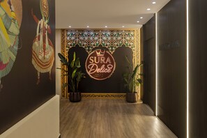 Een hal met een decoratieve wand, een neonbord met de tekst 'SURA Delight' en potplanten.