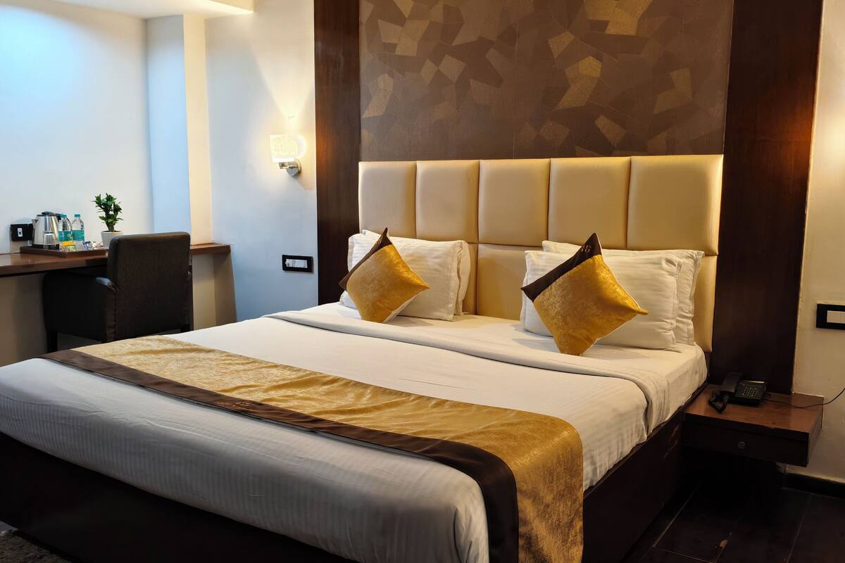 Une chambre d’hôtel avec un grand lit, deux coussins décoratifs dorés, un bureau avec une chaise et un téléphone fixé au mur.
