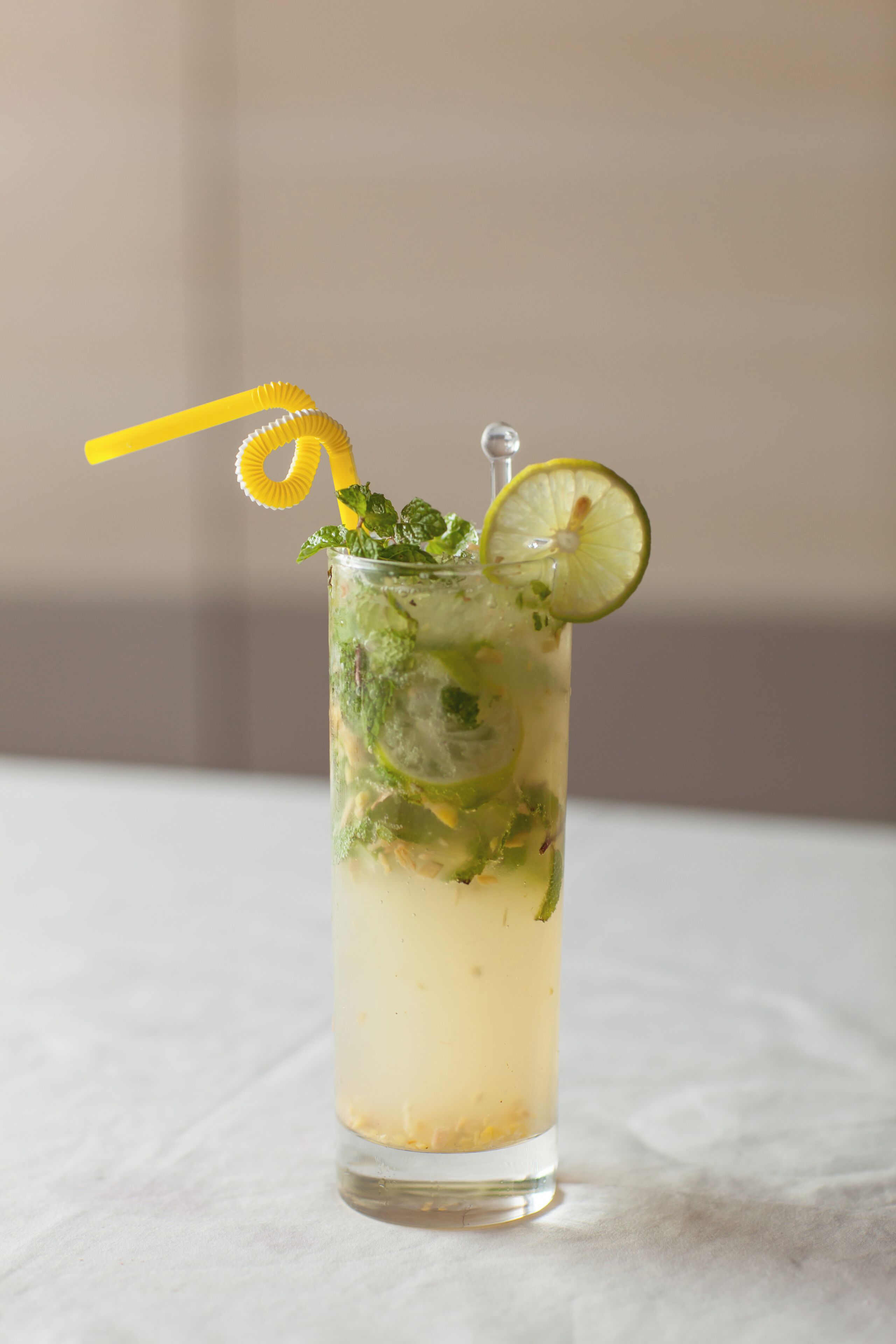Un bicchiere alto con una cannuccia gialla, una fetta di lime e una guarnizione di menta.