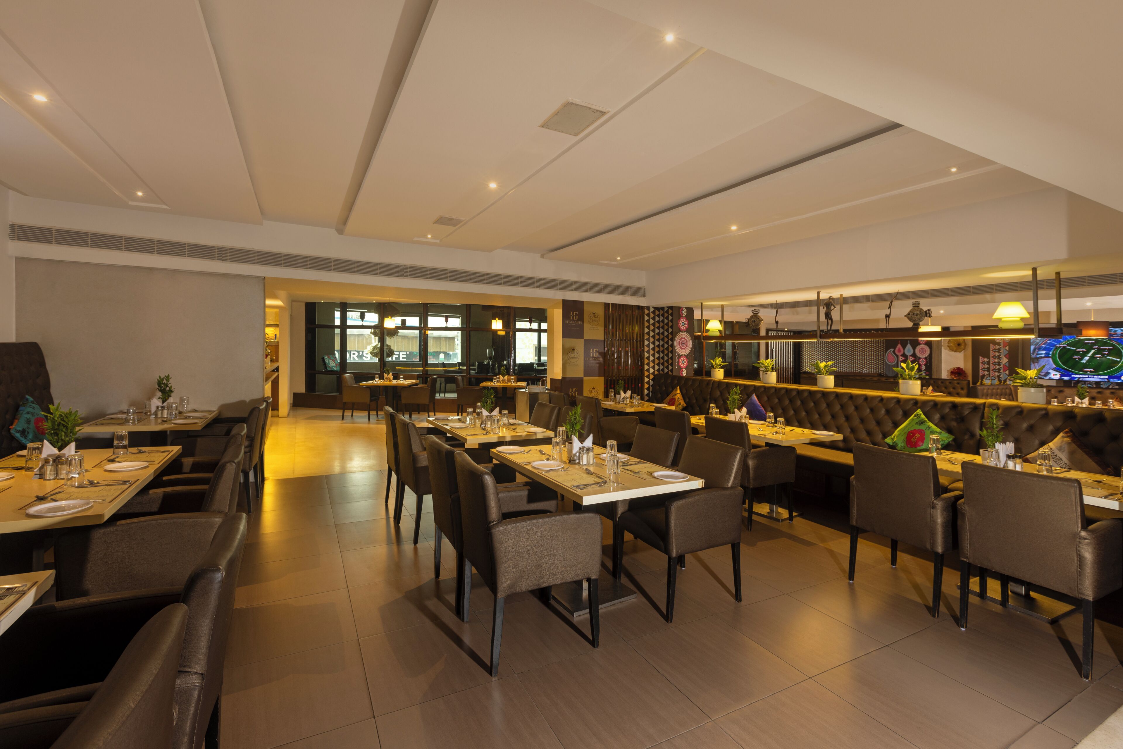 A modern restaurant with multiple dining tables and chairs, a bar area, and a view of the street outside.