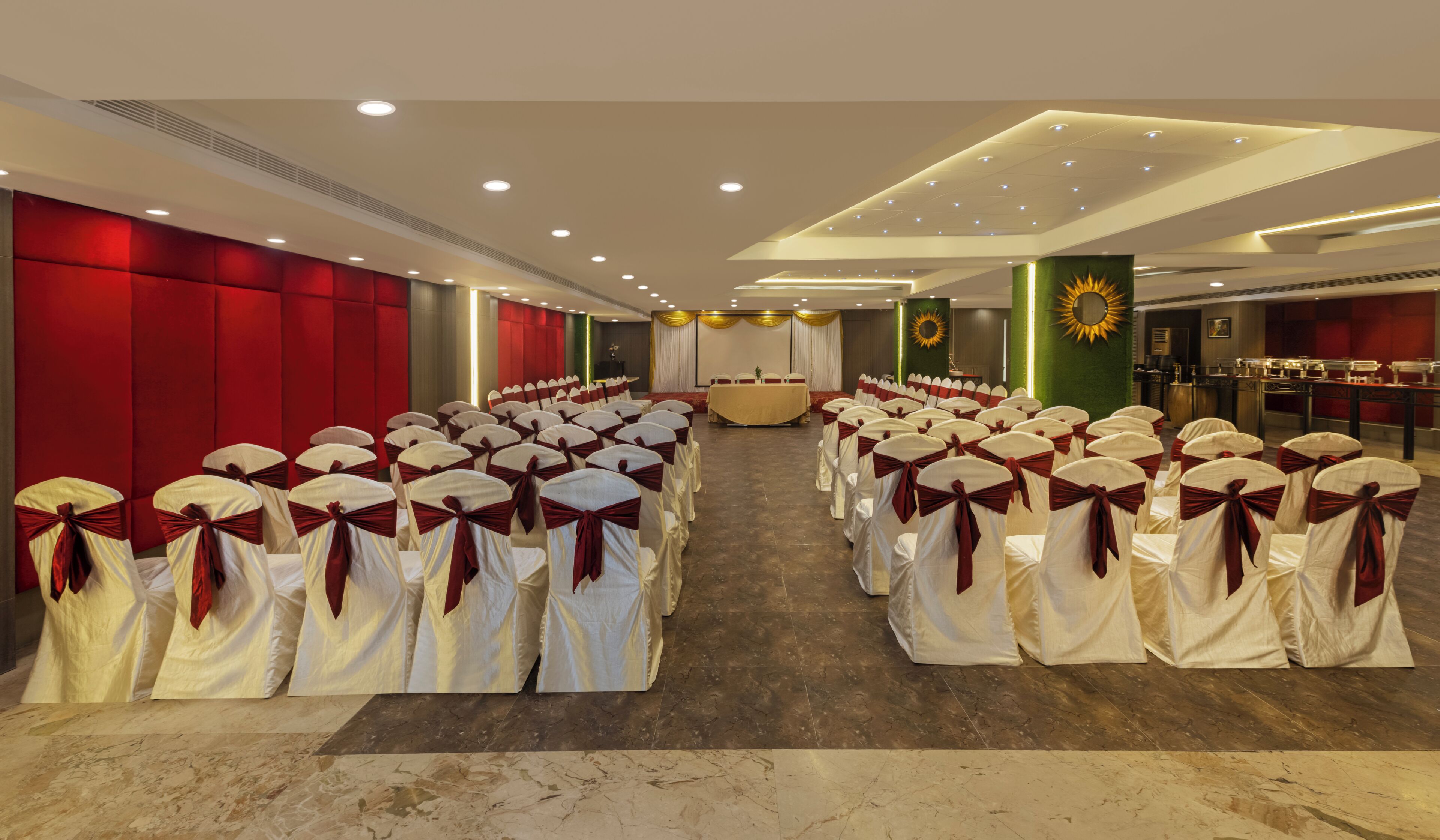 Un salón de conferencias con filas de sillas, un escenario y una zona de buffet.