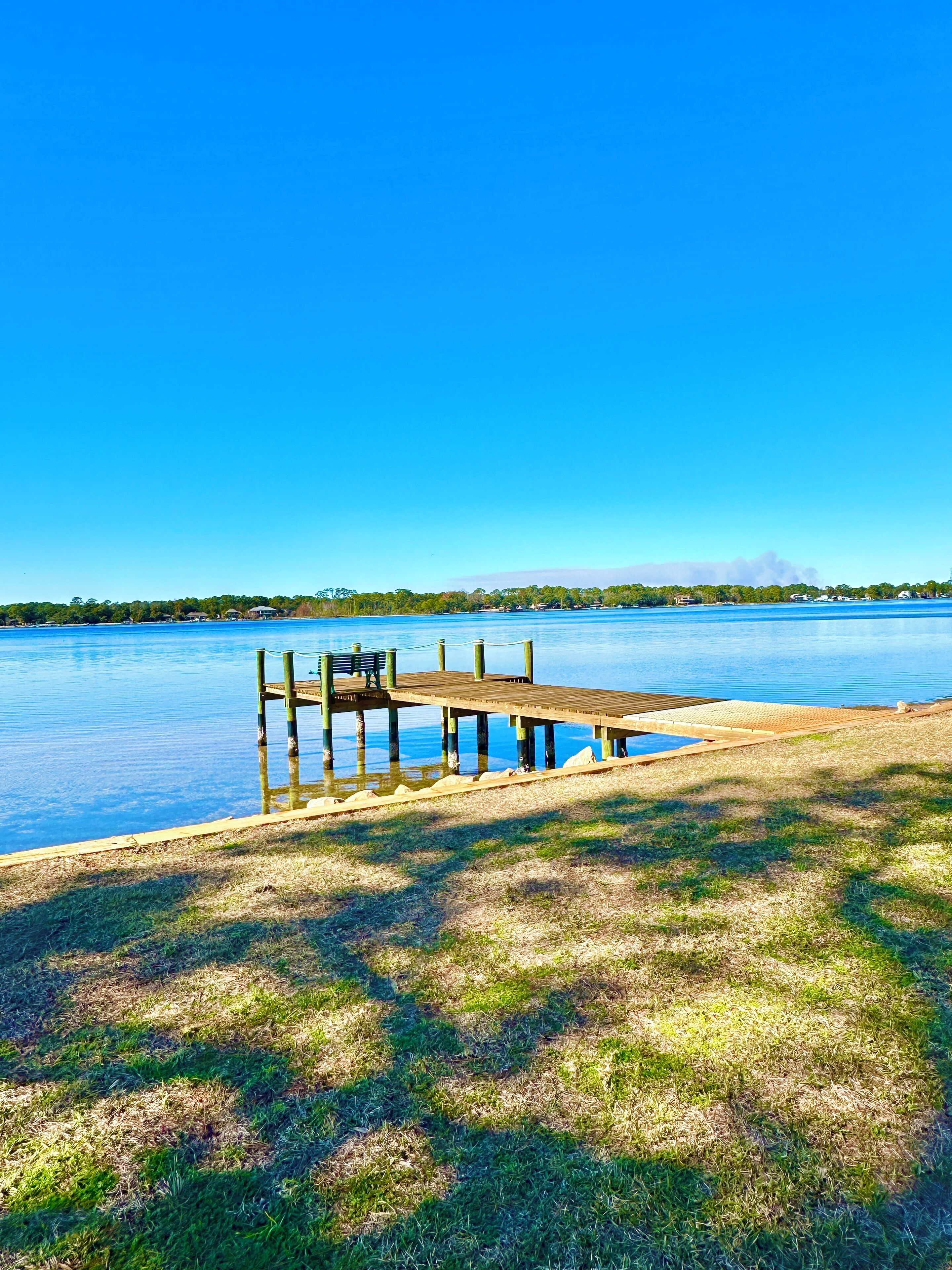 A wooden dock extending into a calm lake with a clear blue sky above.