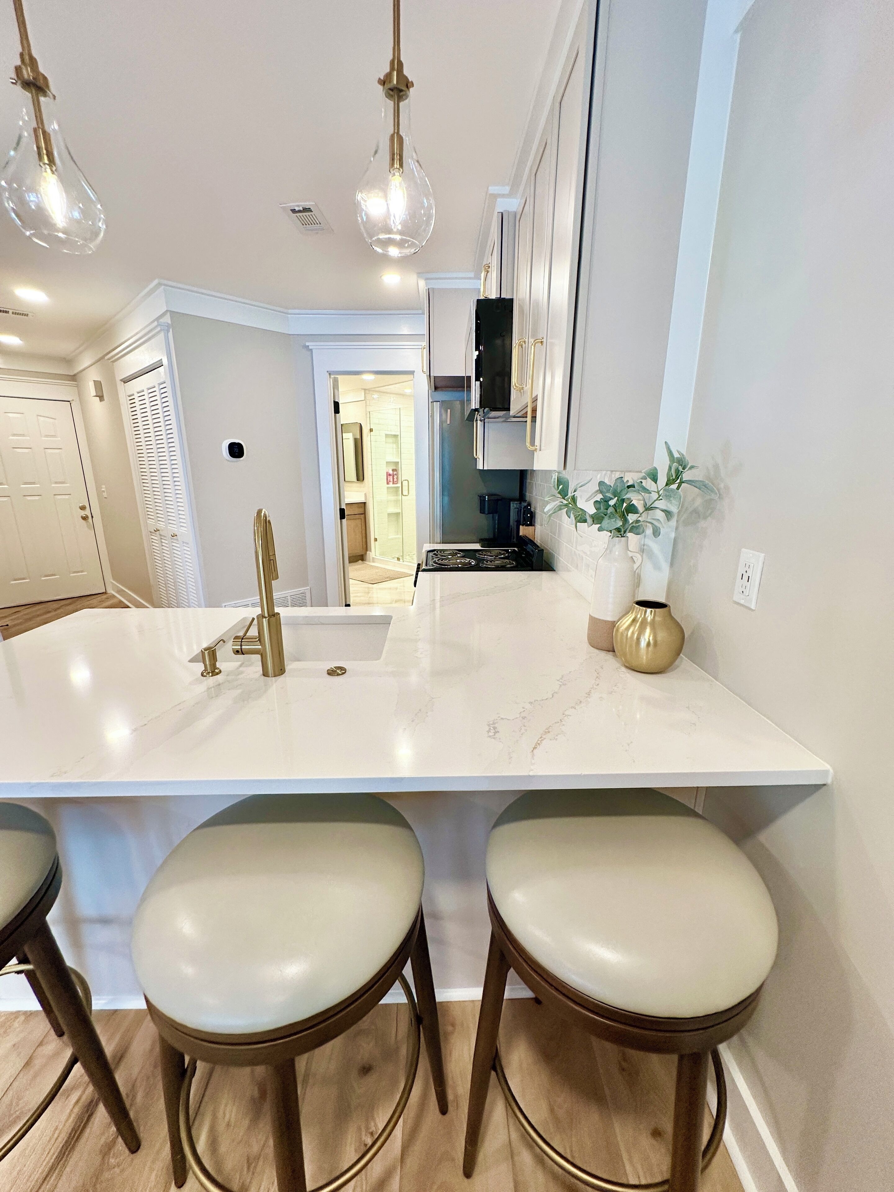 A modern kitchen with a central island, bar stools, pendant lighting, and a view into the adjacent bathroom.