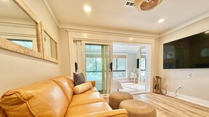 A modern living room with a leather sofa, two ottomans, a large flat-screen TV, and a large mirror on the wall.