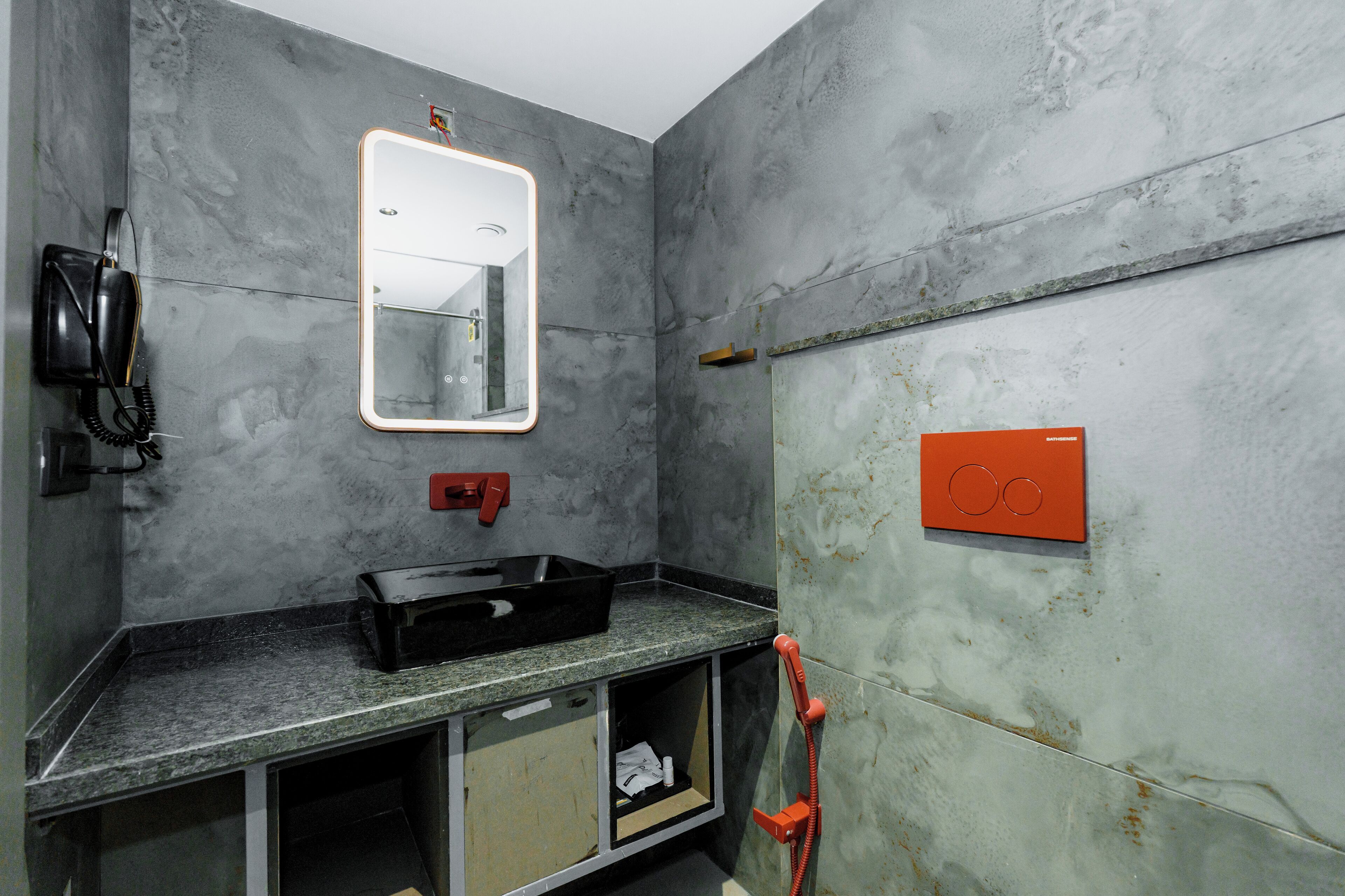 Une salle de bain avec un mur en marbre, un miroir, une valise noire, un téléphone rouge et un porte-serviettes.