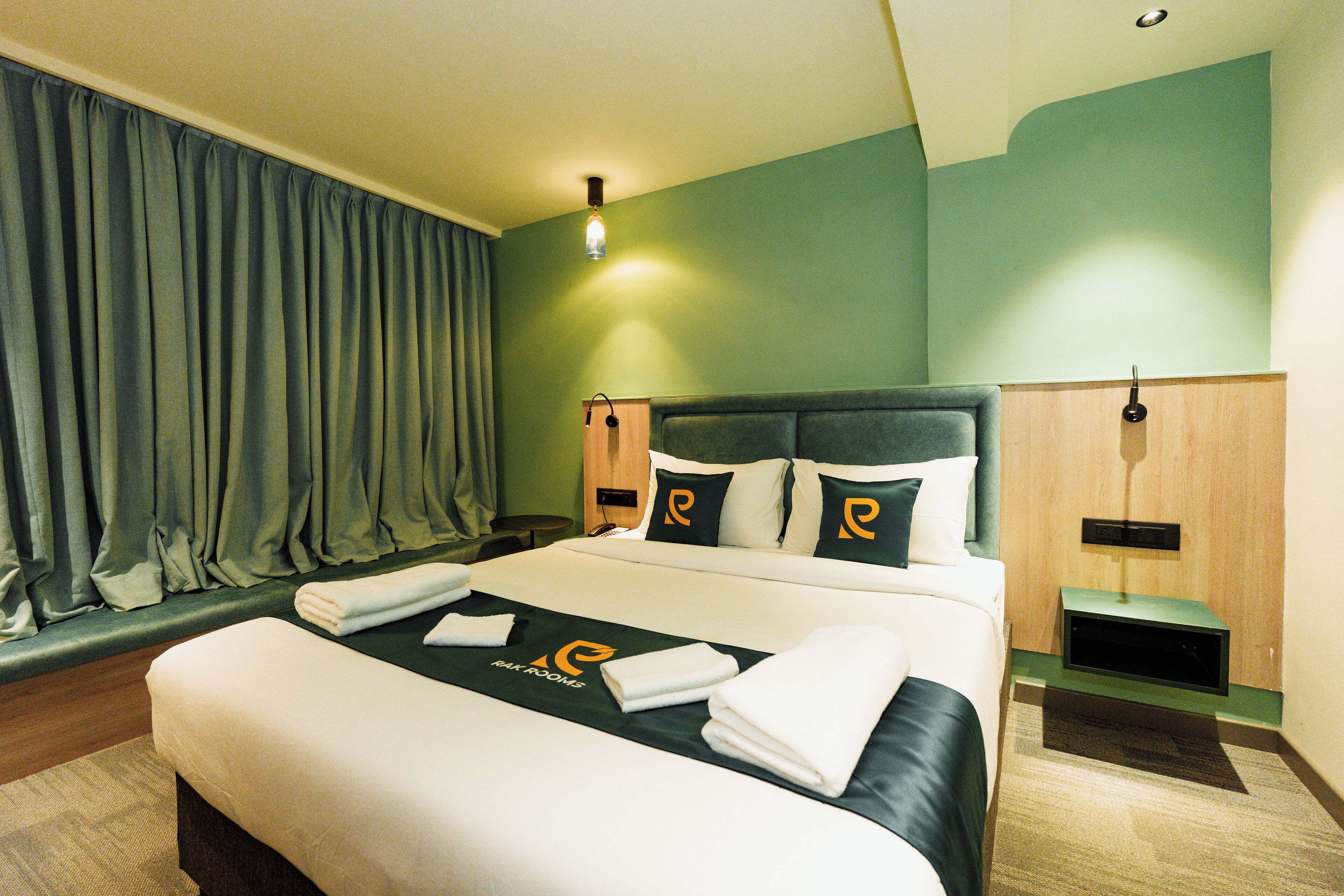 A hotel room with a neatly made bed, a bedside table, a nightstand, and a wall-mounted lamp.