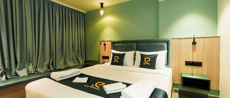 A hotel room with a neatly made bed, a bedside table, a nightstand, and a wall-mounted lamp.