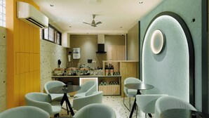 A modern kitchen with white appliances, a ceiling fan, and a dining area with light-colored chairs and tables. - GP Xpress Inn by RAK Rooms (Mangaluru)