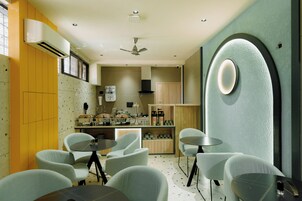 Una cocina moderna con electrodomésticos blancos, ventilador de techo y zona de comedor con sillas y mesas de colores claros.