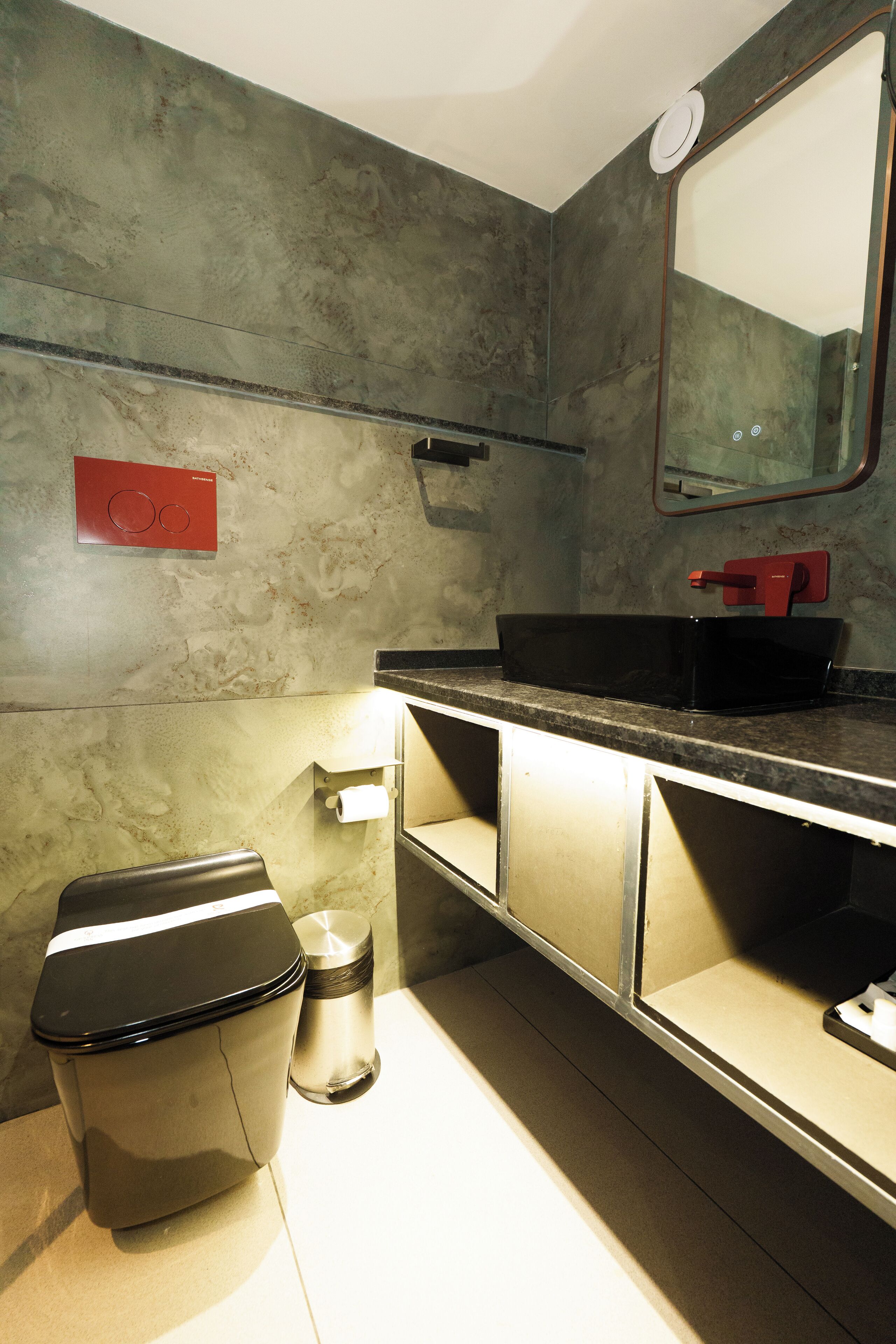 A modern bathroom with a black sink, a toilet, and a trash bin.