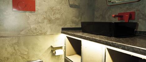 Une salle de bain moderne avec un lavabo noir, des toilettes et une poubelle.