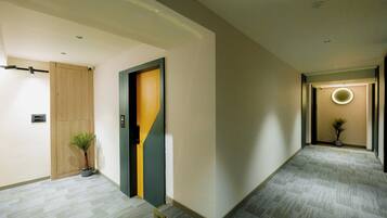 Un pasillo moderno con puerta de madera, una planta en maceta y una lámpara circular.