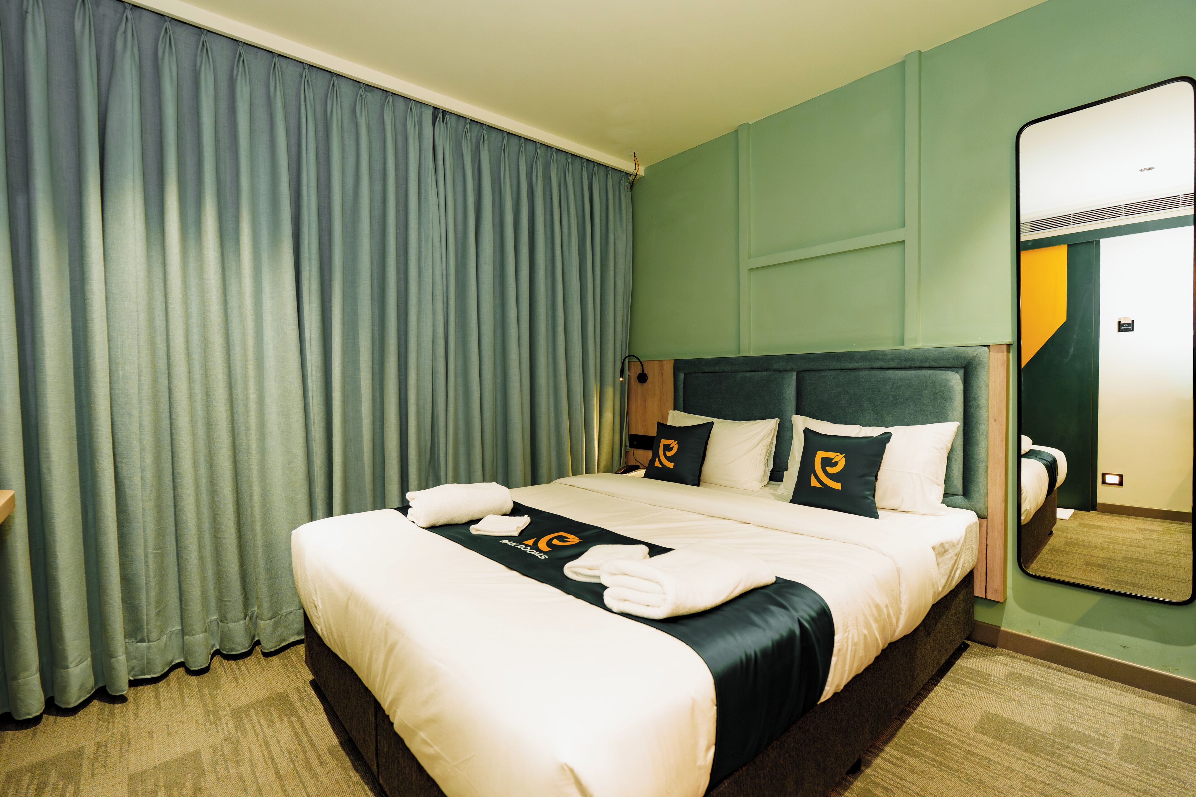 Habitación de hotel con una cama grande, cabecera, espejo y cortina.