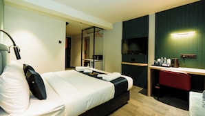 A hotel room with a bed, bedside table, desk, chair, and a mirror. - GP Xpress Inn by RAK Rooms (Mangaluru)