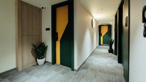 A hallway with a wooden door, a green and yellow door, and a potted plant. - GP Xpress Inn by RAK Rooms (Mangaluru)