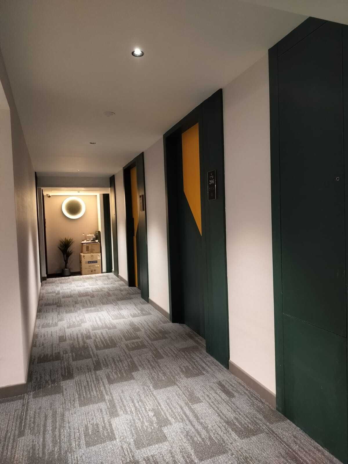 A hallway with carpeted flooring, dark green doors, and a circular light fixture on the ceiling.