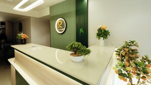 A reception desk with a logo, a potted plant, and a wall-mounted sign. - GP Xpress Inn by RAK Rooms (Mangaluru)