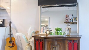 Un salon avec un téléviseur à écran plat fixé au mur, un meuble en bois agrémenté de touches de rouge, une guitare et une table basse en verre sur laquelle sont posés des magazines.
