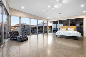 A spacious bedroom with a large bed, a leather chair, and floor-to-ceiling windows offering a view of the outside. - Striking Luxury Home with Garden & BBQ (Margate)