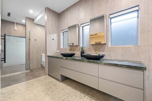 A modern bathroom with a large vanity, two sinks with black bowls, a mirror above each sink, and a shower area with a glass door. - Striking Luxury Home with Garden & BBQ (Margate)