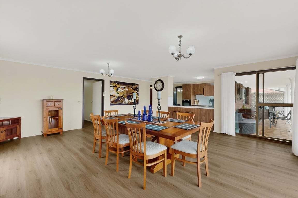 A dining area with a wooden table and chairs, a chandelier, and a view of the kitchen and outdoor patio.