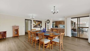 Un comedor con mesa y sillas de madera, una araña y vistas de la cocina y el patio exterior.