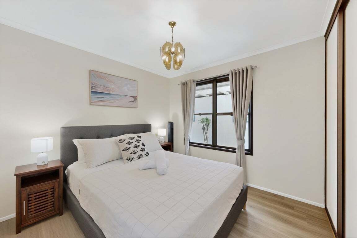 Une chambre à coucher bien rangée, avec un grand lit, des tables de chevet, une fenêtre avec des rideaux et un luminaire au plafond.