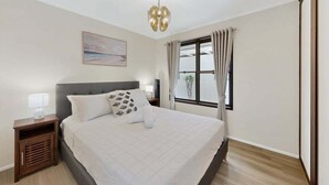 Un dormitorio ordenado con una cama grande, mesitas de noche, una ventana con cortinas y una lámpara en el techo.