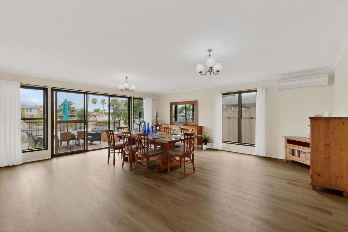 A spacious dining area with a wooden table and chairs, large sliding glass doors leading to an outdoor patio, and a wooden cabinet.