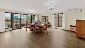 Un comedor amplio con una mesa y sillas de madera, amplias puertas correderas de vidrio que dan a un patio exterior, y un armario de madera.