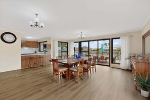 Un comedor amplio con una mesa y sillas de madera, una cocina al fondo y grandes puertas correderas de cristal que dan a un patio exterior.